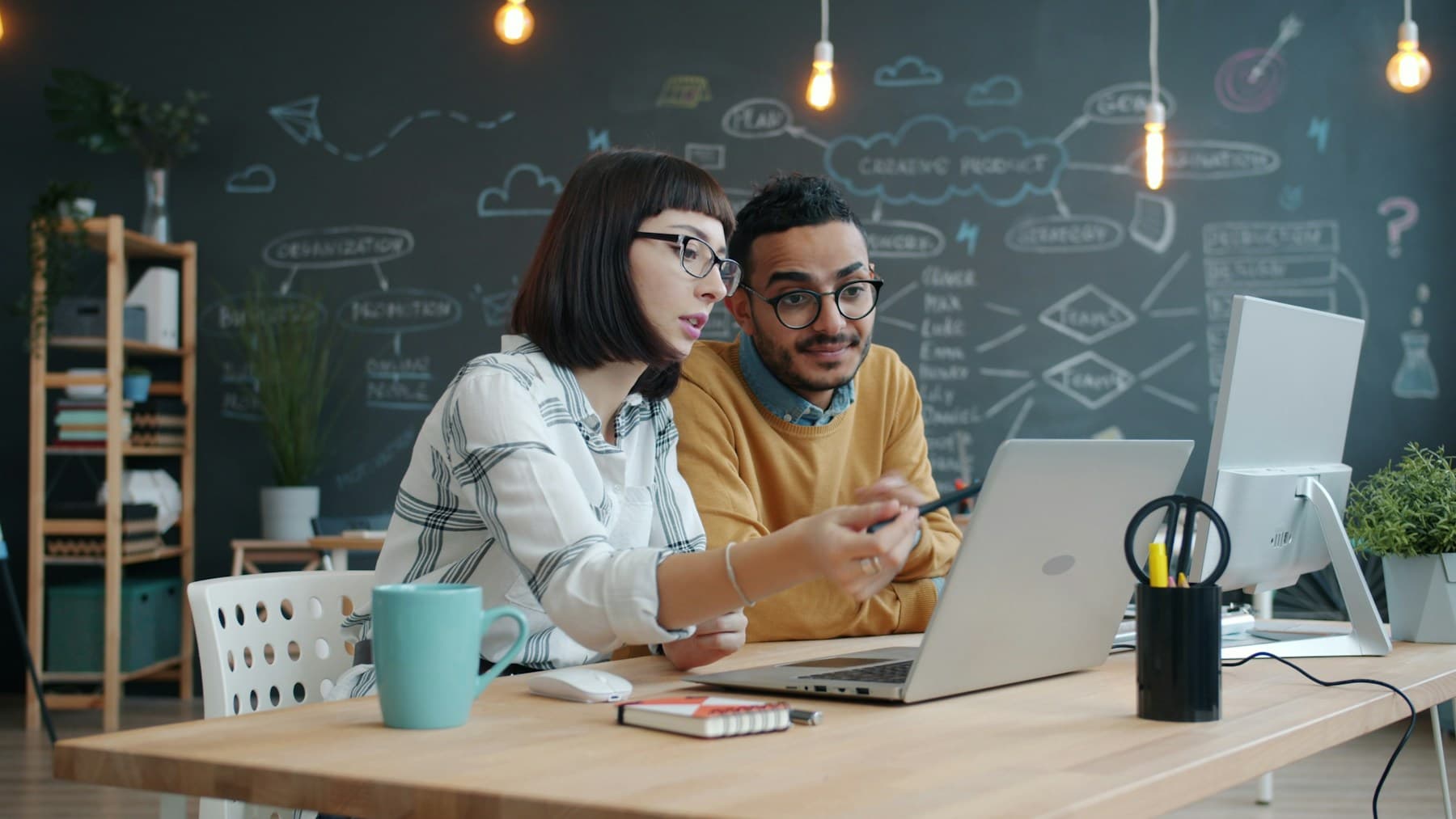 Two colleagues at a desk looking at the same laptop screen
